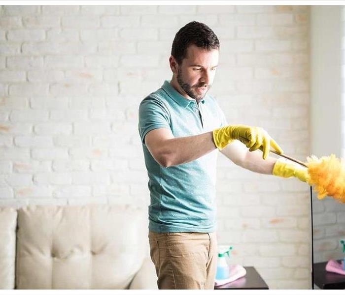 a man dusting furniture in home wearing blue shirt 